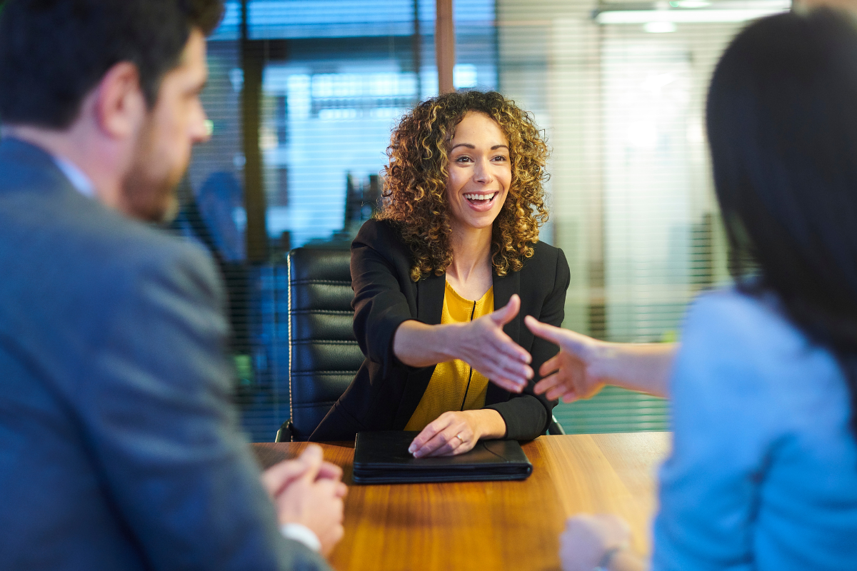 Woman in a yellow top is at an interview and is shaking hands with a female interviewer.