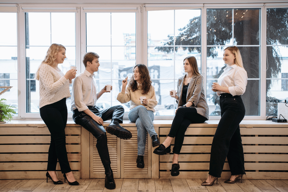 Coworkers holding coffee mugs, talking in front of a window