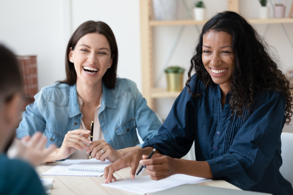 two women smiling over a table with papers