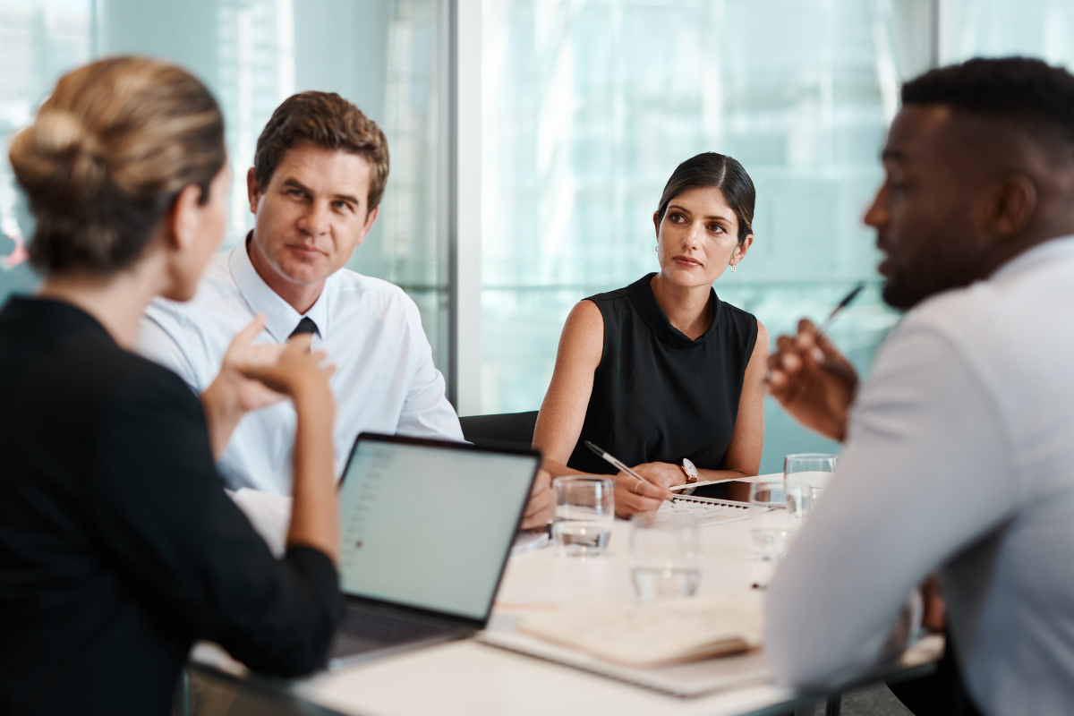 2 women and 2 men sitting around a table having a meeting with laptop and papers