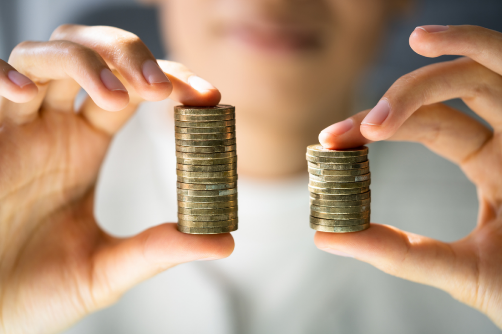 Woman holding a stack of coins between her pointer finger and thumb in each hand. One stack is taller than the other.